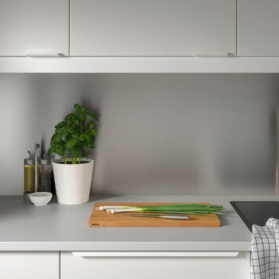 Minimalist grey kitchen counter. Small potted plant, oil bottles, knife, scallions, and cutting board with LYSEKIL wall panel.