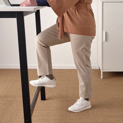 A person leans on a high conference table with a footrest, showcasing its use for both sitting and standing.