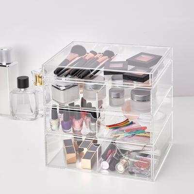Clear acrylic storage box with four drawers holding makeup items, including nail polishes, makeup brushes, and lipsticks.