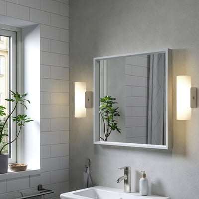 Modern bathroom with large NISSEDAL mirror flanked by lights. White sink, green plant, grey tiles. Mirror reflects room, adding depth.