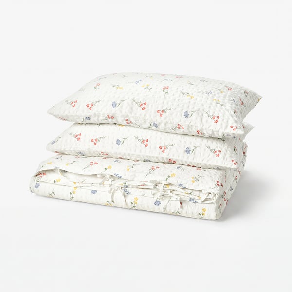 Floral duvet and pillow set, white with red, yellow, blue flowers, soft cotton/viscose blend, seersucker texture, tied neatly.