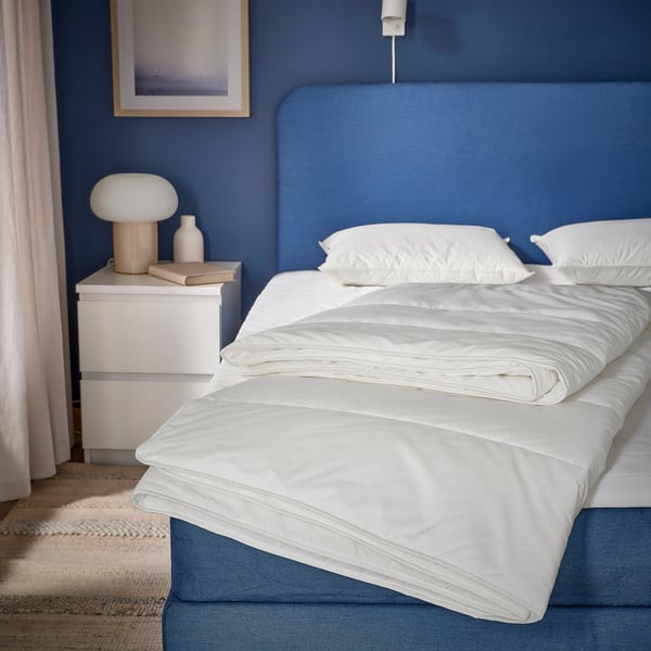 Blue bed with SKOGSFRÄKEN duvet, pillows, bedside lamp, books.