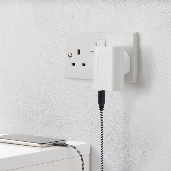 A wall-mounted charger with three usb ports charging a smartphone. Its compact, charging three devices simultaneously.