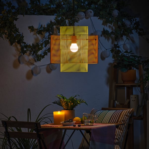 Small outdoor table set with striped chairs, hanging light, plants, and candle, creating a cosy evening ambiance.
