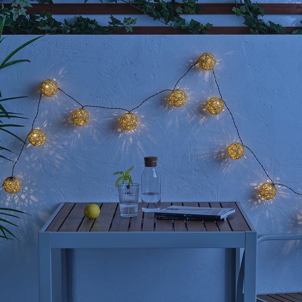 Gold lights warm a patio, illuminating a table with lemon, glass, carafe, and magazine.