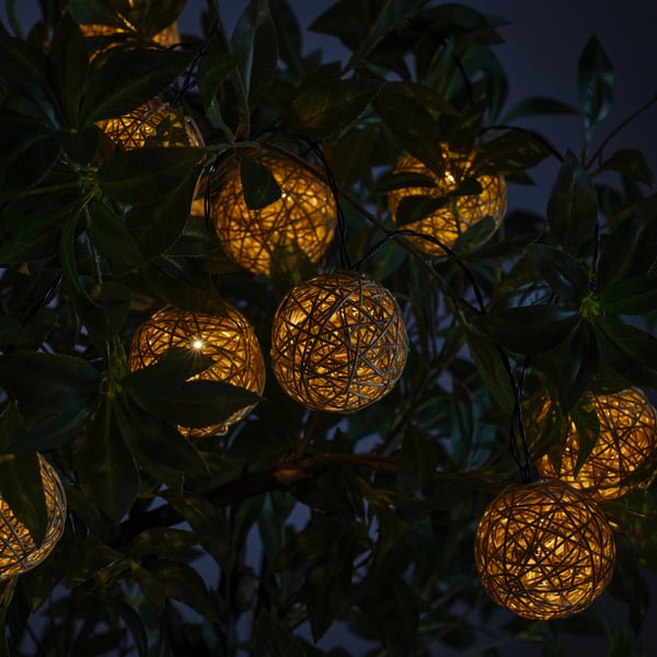 Golden sphere lights hang in a green tree at dusk, emitting a warm glow.