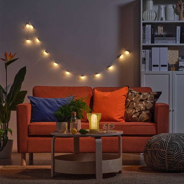 Cosy living room with orange sofa, string lights, coffee table, and bookshelf.