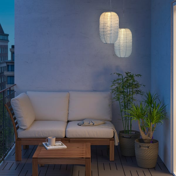 Cosy balcony with SOLVINDEN lanterns, white cushioned sofa, wooden table, and plants.