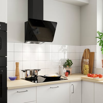 Modern kitchen with white cabinets, black hood, and wooden counter. A skillet with food sits on the cooktop.