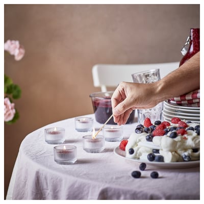 Hand lights candle on table with dessert, lit candles, glasses, and red striped napkins.
