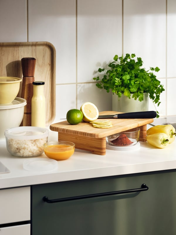 Wooden cutting board with knife, lime, lemon, seasonings, and vegetables on kitchen counter.