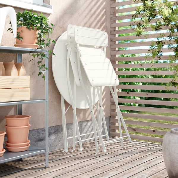Balcony with 3 white metal foldable chairs, wooden pots, and a shelving unit.