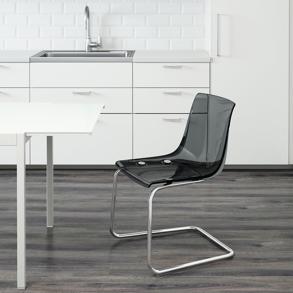 Modern kitchen with sleek cabinets and sink. In foreground, transparent TOBIAS chair with flexible seat and back, designed to blend with surroundings.