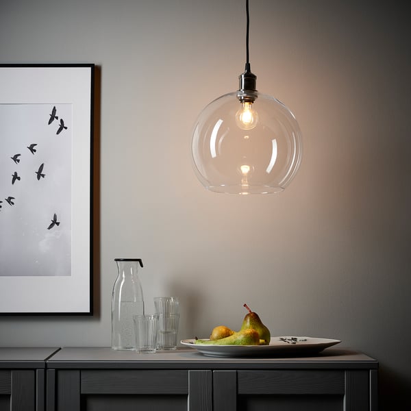 Hanging light with glass shade, illuminated bulb, wall art, vase, glasses, and plate with fruits on table.