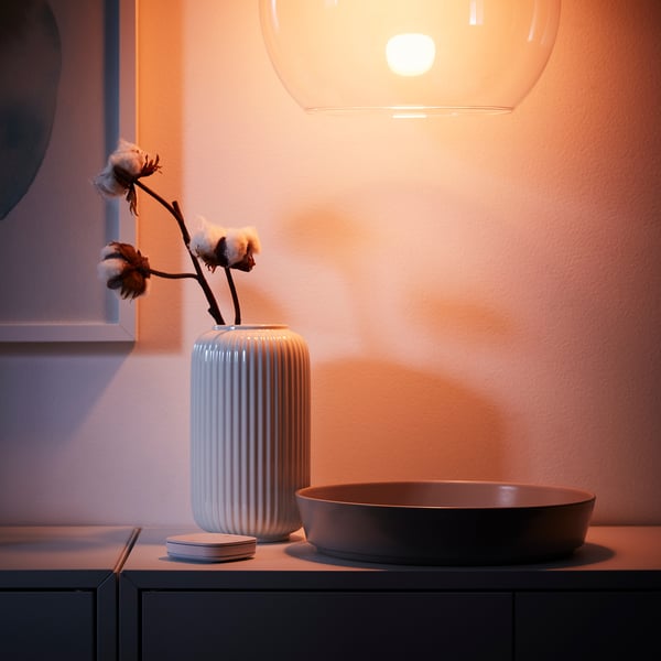 Modern setting: white ribbed TRÅDFRI vase with cotton stems, black bowl, under warm glowing light.