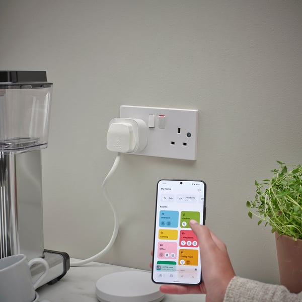 Hand holds smartphone with TRETAKT app controlling kitchen plug; blender & plant beside.