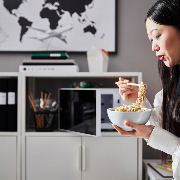 Person eating noodles at TROTTEN white storage desk. Desk has adjustable feet, lockable storage, and metal tube construction.