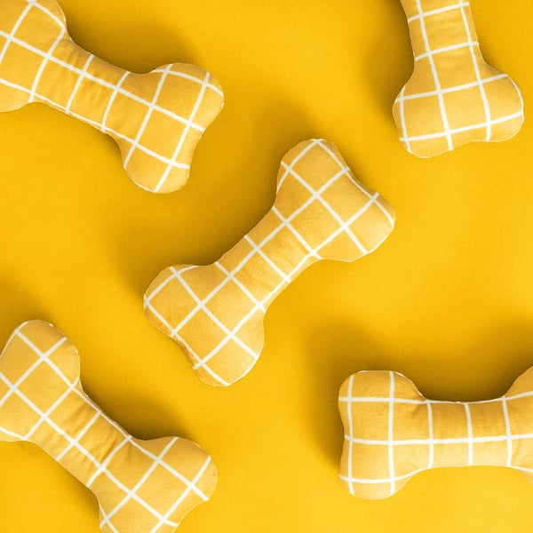 Bone-shaped dog toys in yellow chequered fabric on yellow background.