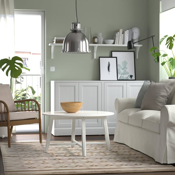 Modern living room with green walls, wood floor, area rug, white furniture, and shelf decor.