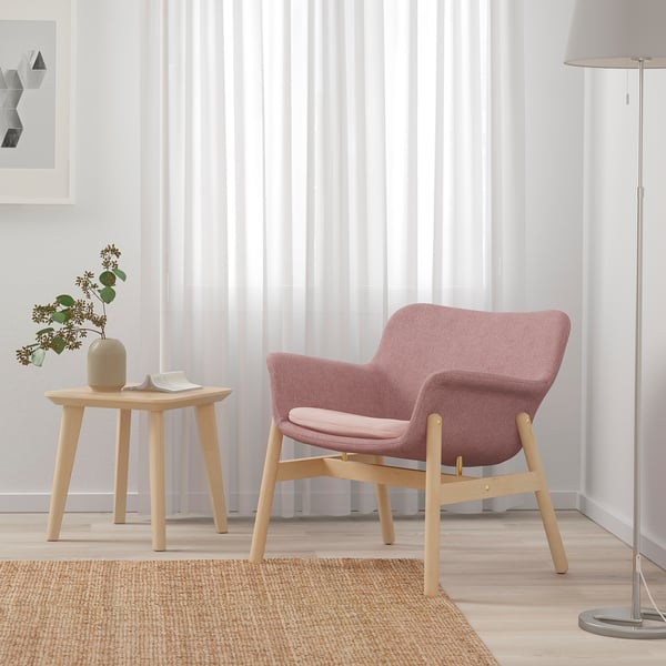 Pinkish-brown VEDBO armchair with soft lines and wooden legs next to a side table, lamp, and jute rug in minimalist room.