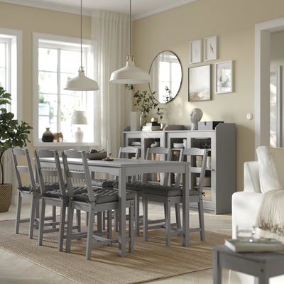 Modern dining room with grey VIPPÄRT chair pads, wooden table, hanging lights, area rug, curtains, window, plants, and wall decorations.