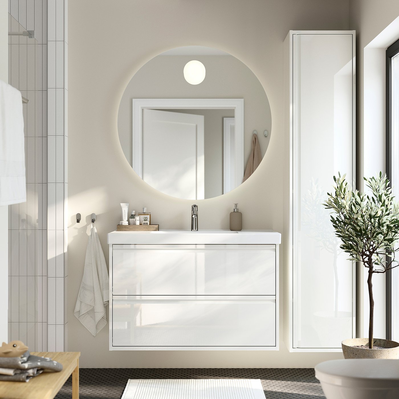 Modern white ÄNGSJÖN bathroom vanity, round mirror, glass doors, sleek handles. Dark floor, green plant.