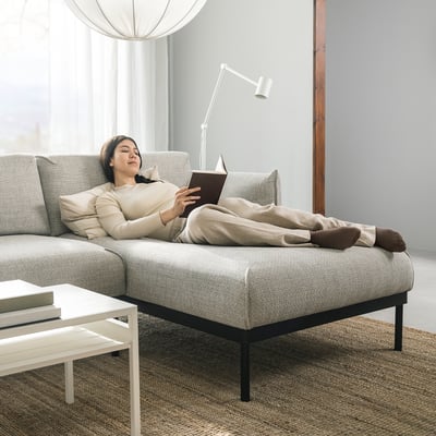 Person relaxes on grey ÄPPLARYD sectional sofa, reading a book. Sofa clean lines, supportive cushions, and a cosy, minimalist design.