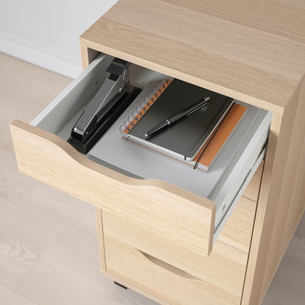 Wooden desk drawer open, revealing a stapler, notebook, and pen inside. Easy access for office organisation.