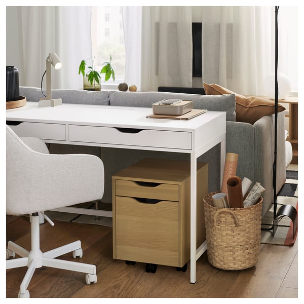 White ALEX desk with drawers and basket, laptop on tray, near sofa in bright room.