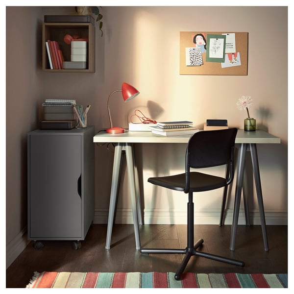 Compact home office with ALEX grey storage unit, white desk, black chair, red lamp, and colourful rug.