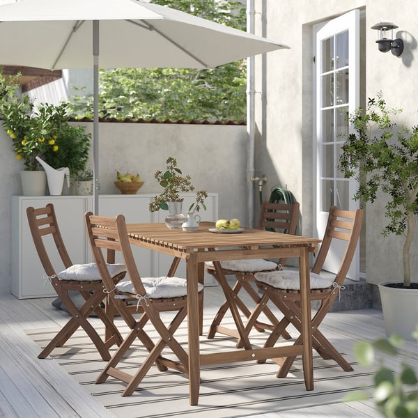 Wooden outdoor table & 4 folding chairs with light grey cushions, on striped rug under white umbrella.