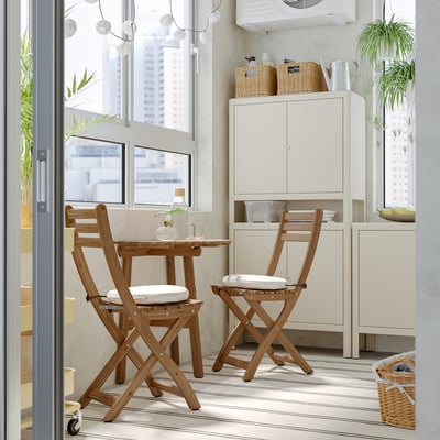 Small, wooden ASKHOLMEN dining set with cushioned chairs fits neatly by large window, beside white cabinet in cosy room.