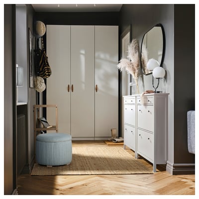 A modern, stylish entryway with a light-colored wardrobe, a storage unit, and a light blue, cylindrical storage ottoman on a jute rug.