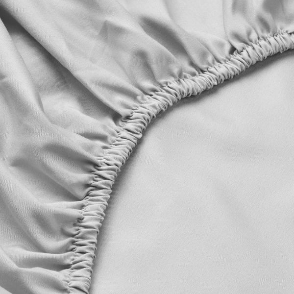 Close-up of a smooth, grey bed sheet with elastic edges. Soft, neatly folded fabric shows quality and comfort.