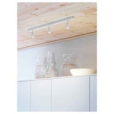 Modern kitchen with white ceiling track lights featuring adjustable spots illuminating clear glass vases on a white cabinet below.