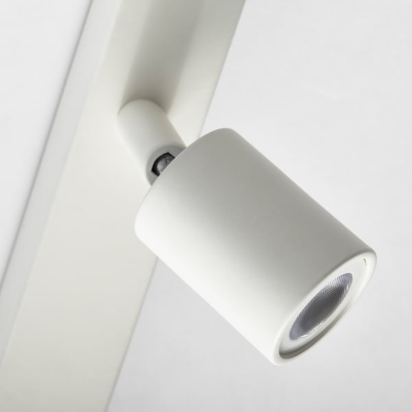 A modern, minimalist ceiling-mounted spotlight. It a sleek, white design with a cylindrical shade, emitting directed light.
