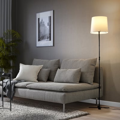 Living room with BARLAST floor lamp providing soft light, grey couch, and black & white photo on dark wall.