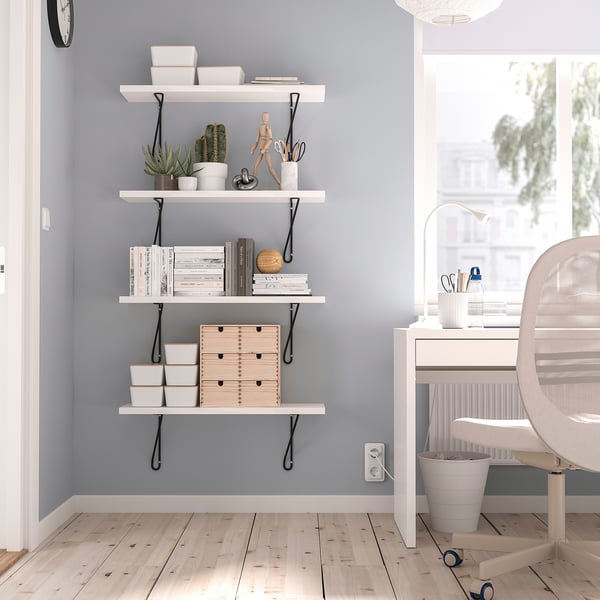 Modern home office with white shelf holding books and plants. Light grey wall and natural light from window.
