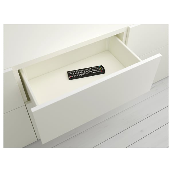 Open drawer of white BESTÅ unit with remote control inside.
