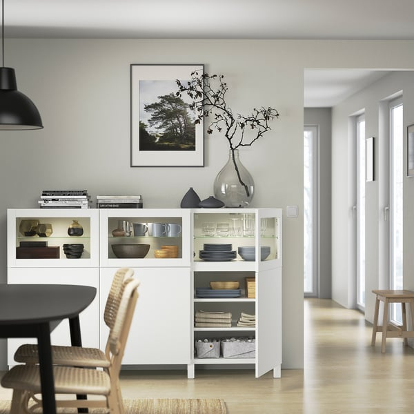 Modern dining room with white BESTÅ sideboard showcasing dishes, decor, and adjustable shelves. Soft-closing doors and glass fronts are visible.