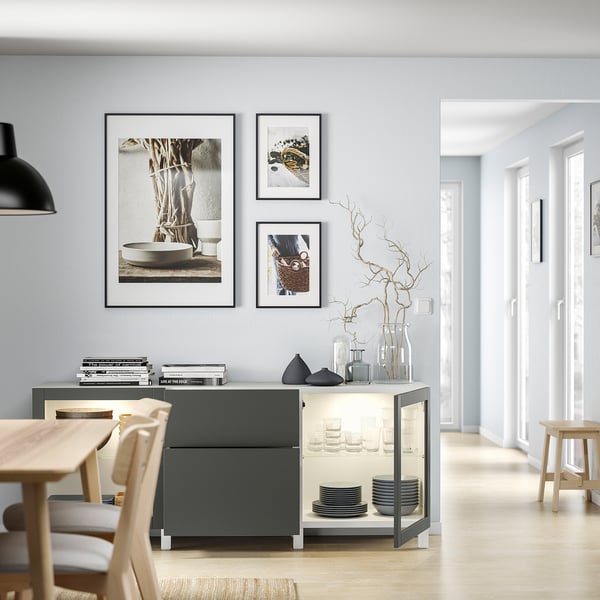 Modern dining area with grey BESTÅ storage unit, white dishes, glass vases, and framed art on wall.