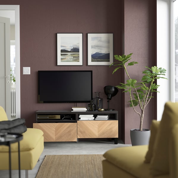 Contemporary living room with BESTÅ tv bench and flat-screen tv, colourful decor, organised cables, and a plant.