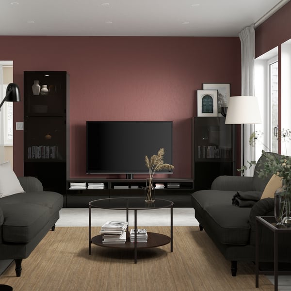 Modern living room with maroon walls, black BESTÅ tv stand, grey sofas, glass coffee table, and floor lamp.