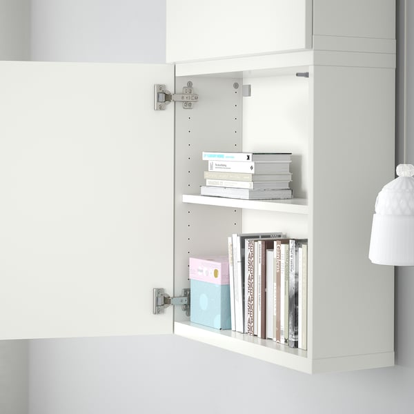 White cabinet with two shelves holding assorted books, mounted on wall with visible hinges.