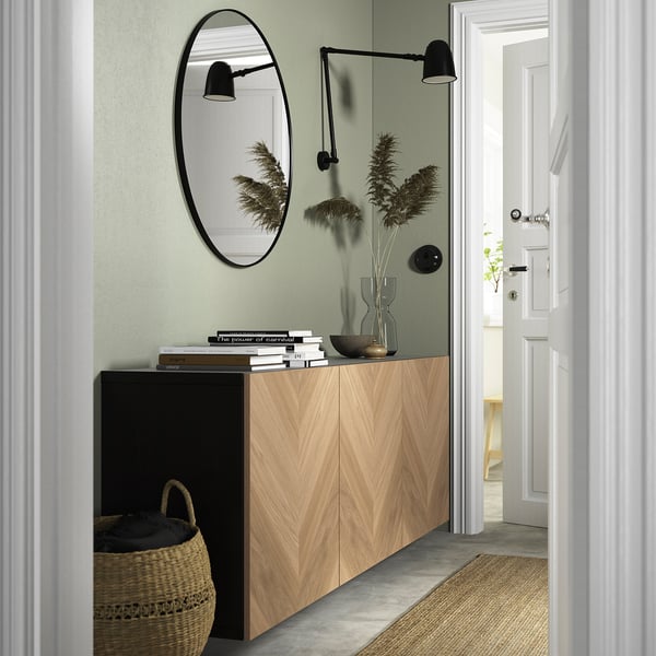 Modern hallway with BESTÅ sideboard. Circular mirror, wall lamps, and a tall basket. Green walls, compact yet functional.