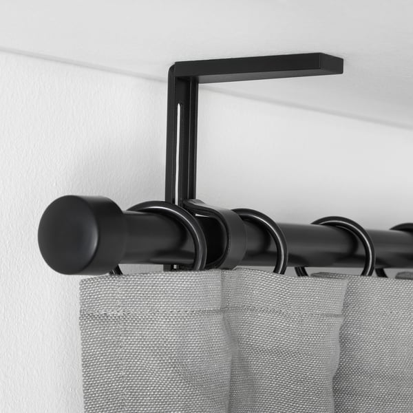 Black curtain rod holder mounted on white wall, holding black rod with grey curtains, demonstrating adjustable positioning.