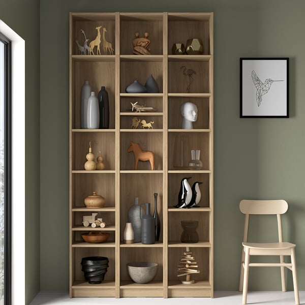Large wooden BILLY bookcase with various decor items on shelves against green wall.