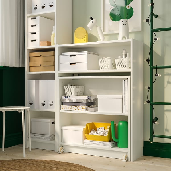 White BILLY bookcase with foldable table, displaying various storage boxes, games, and decor items.