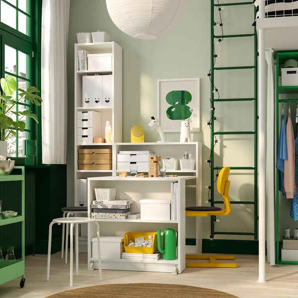 White BILLY bookcase with foldable table, green cabinets, window, ladder, yellow chair, cactus.