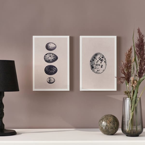 Two framed prints on wall. Left: lamp, right: vase with dried plants. Stone on table.